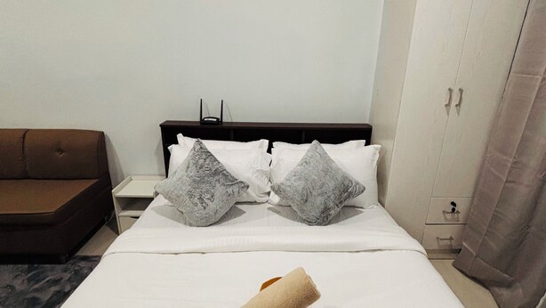 Quarto de hotel com uma cama, mesa de cabeceira, guarda-roupa e um sofá marrom.