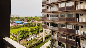 Um edifício residencial de vários andares com varandas, um pátio interno e vista para um parque verde e outros edifícios ao fundo.