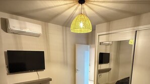 Une chambre à coucher comprenant un lit, un téléviseur fixé au mur, un luminaire au plafond et un miroir.