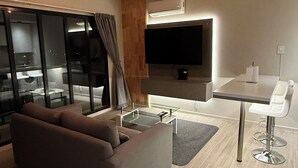 Un salon moderne comprenant un canapé, une table basse en verre, un téléviseur fixé au mur et un coin repas avec une table et des chaises blanches.
