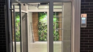 A hotel entrance with a glass door, a keypad security system, and a tactile paving mat. - New England Ecoloft Studios (Kyiv)