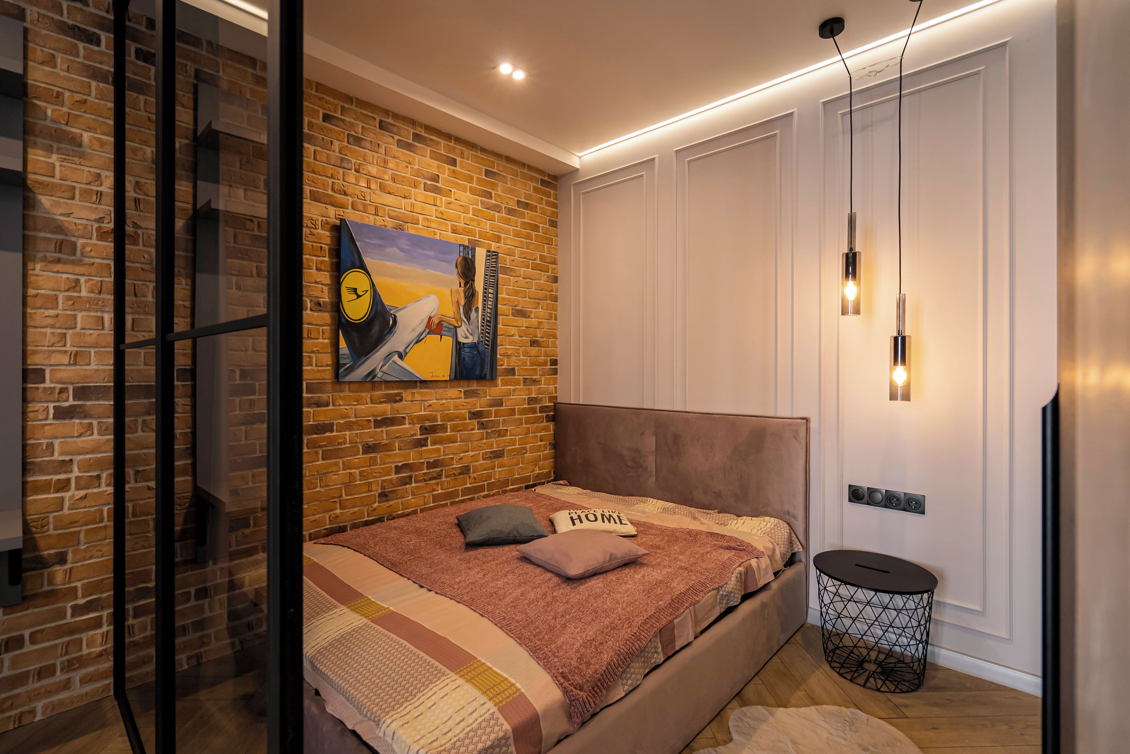 A modern bedroom with a brick wall, a large bed, a painting, and a small side table.