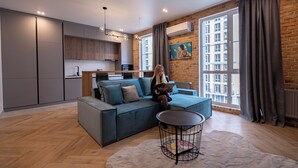 A modern living room with a sofa, a coffee table, and a view of a cityscape through large windows. - New England Ecoloft Studios (Kyiv)