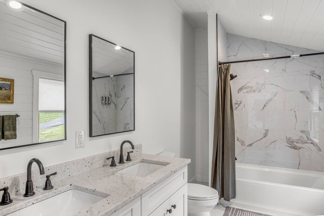 A modern bathroom with a double sink vanity, a large mirror, a bathtub with a marble surround, and a shower curtain.