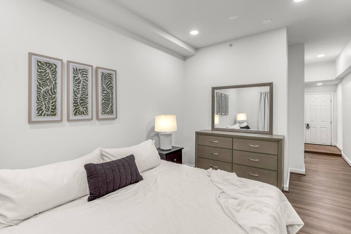 A bedroom with a bed, a dresser, a nightstand, a mirror, and three framed wall art pieces.