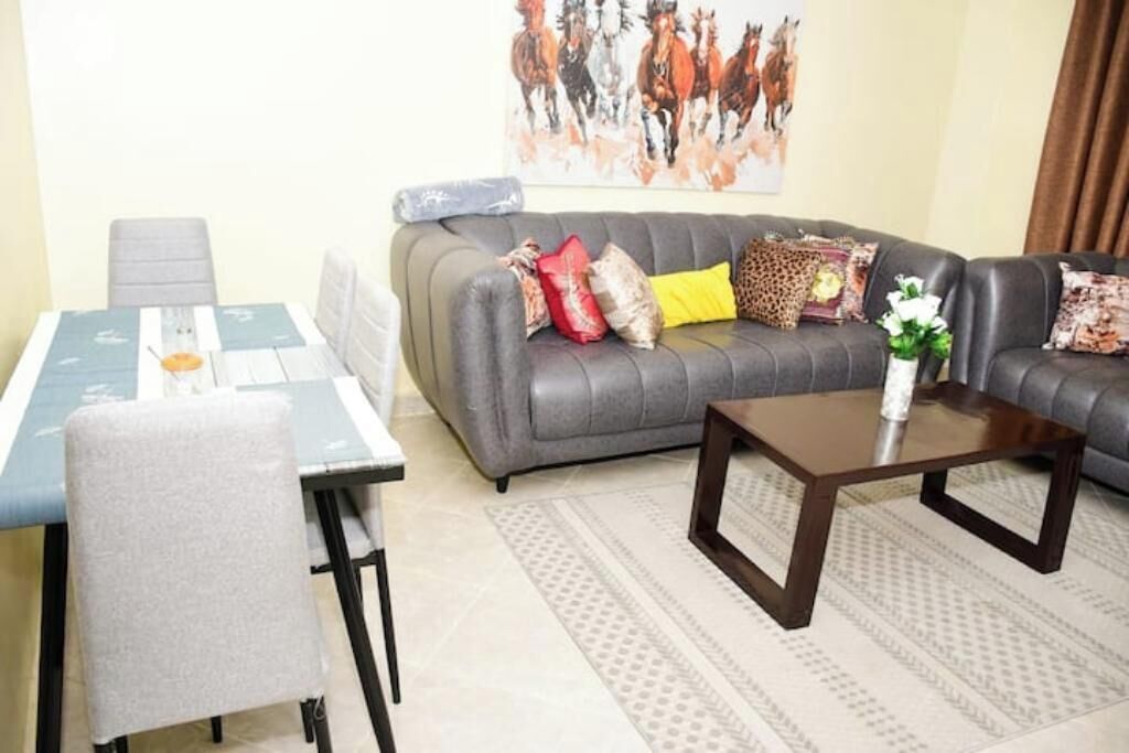 Ein Wohnzimmer mit grauem Sofa, einem Couchtisch, einem Esstisch mit Stühlen und einem Bild von Pferden an der Wand.