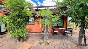 A patio with stone flooring, a pergola, and two wicker chairs.