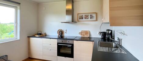 A compact kitchen with a black countertop, stainless steel sink, and a built-in oven. There is a window providing a view of the outdoors.