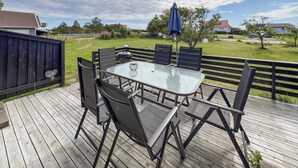 An outdoor deck with a glass-top table and black chairs, surrounded by a wooden deck and a metal railing.