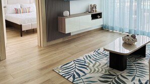 Un salon moderne comprenant un lit, un téléviseur, une table basse et une grande fenêtre avec des rideaux.
