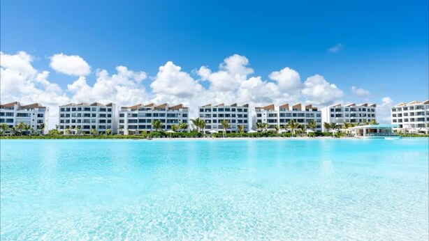 Un complexe hôtelier comprenant plusieurs bâtiments blancs, une piscine à l’eau cristalline et un cadre tropical agrémenté de palmiers.