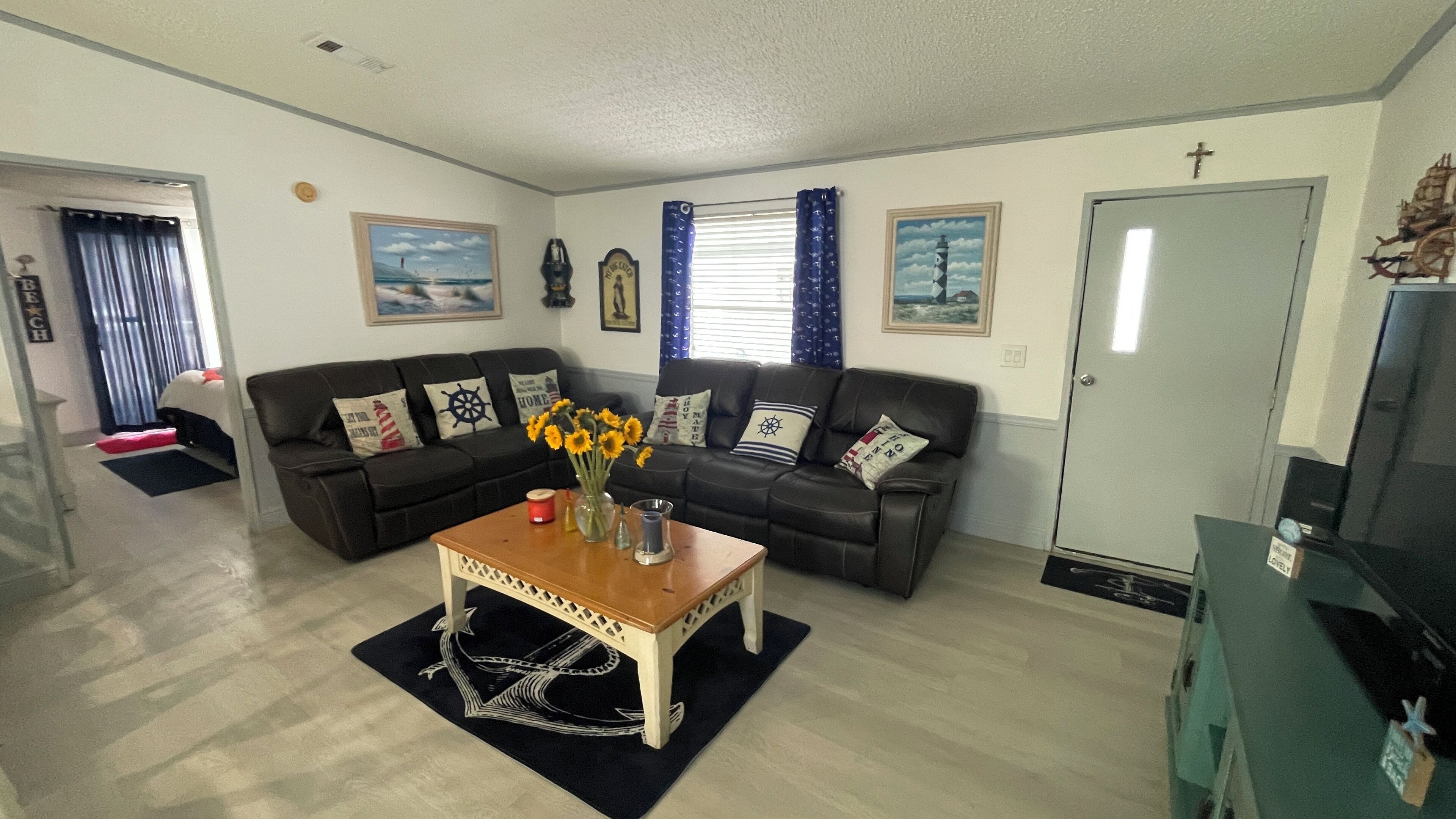 Ein Wohnzimmer mit einer schwarzen Ledersofa, einem Couchtisch mit einer Vase voller Sonnenblumen und einer Tür mit einem Kreuz an der Wand.