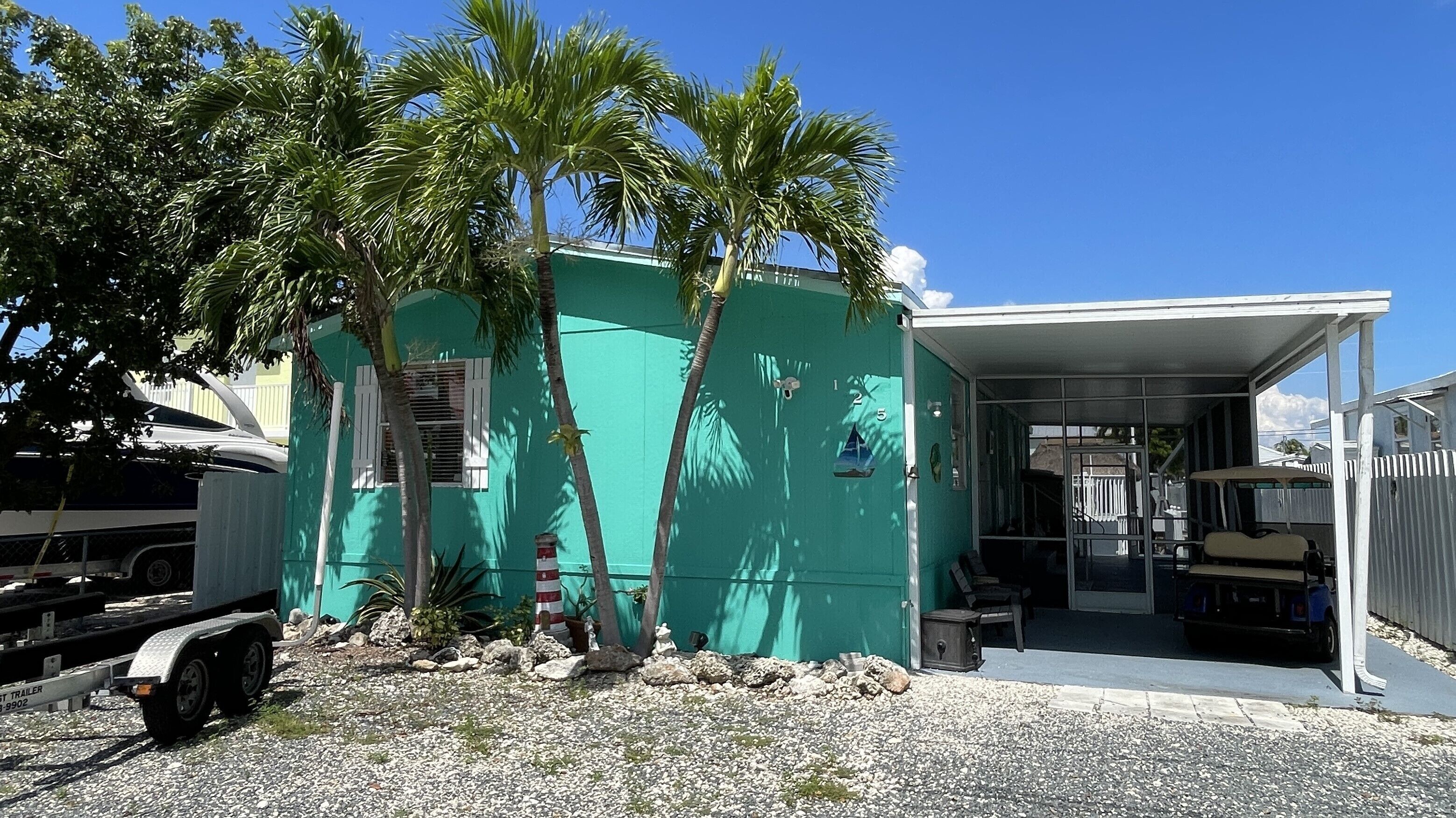 A small, single-story building with a green exterior, a covered porch area, and a gravel driveway.