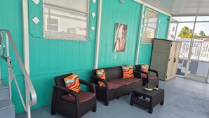 Uma área de estar ao ar livre coberta, com mobiliário de vime e almofadas coloridas, uma escadaria e vista para o exterior.