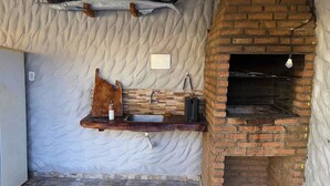 A rustic kitchen with a brick oven, a wooden shelf with a knife block, and a fish mounted on the wall. - MHV Milagres - Casa Naru (Passo de Camaragibe)