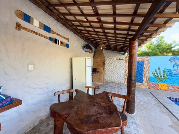 Un espacio de descanso al aire libre con mobiliario de madera rústica, pared de ladrillo y un mural de delfines.