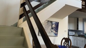 A staircase with dark wooden railings leading to a second floor, a dining area with a wooden table and chairs, and a kitchen area with white cabinets and a microwave. - Lovely 3-bedroom house with loft in Burlington (Burlington)