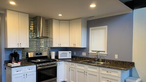 A modern kitchen with white cabinets, stainless steel appliances, a granite countertop, and a window with blinds. - Lovely 3-bedroom house with loft in Burlington (Burlington)