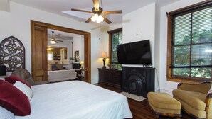 A bedroom with a bed, a television, a chair, a fireplace, and a large window. - Historic Downtown Loft A (Pensacola)