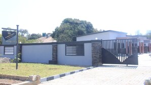 A gated entrance with a sign, a paved pathway, and a building with a modern design. - Founders Apartments (Kabwe)