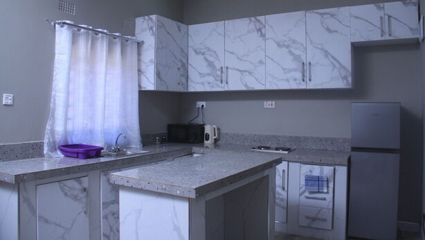A kitchen with marble cabinets, a microwave, a refrigerator, and a purple dish rack. - Founders Apartments (Kabwe)