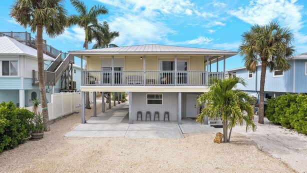 A two-story beachfront house with a balcony, palm trees, and a gravel driveway. - Walk To Beach, North End Restaurants, Night Life Steps Away! (Fort Myers Beach)