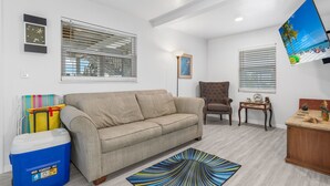A living room with a beige sofa, a brown armchair, a coffee table, and a TV mounted on the wall. - Walk To Beach, North End Restaurants, Night Life Steps Away! (Fort Myers Beach)