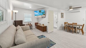 A living room with a sofa, TV, dining table, and chairs. - Walk To Beach, North End Restaurants, Night Life Steps Away! (Fort Myers Beach)