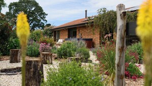 A brick house with a tiled roof, surrounded by a garden with various plants and a wooden fence. - Tuscan Farmhouse (Don Valley)
