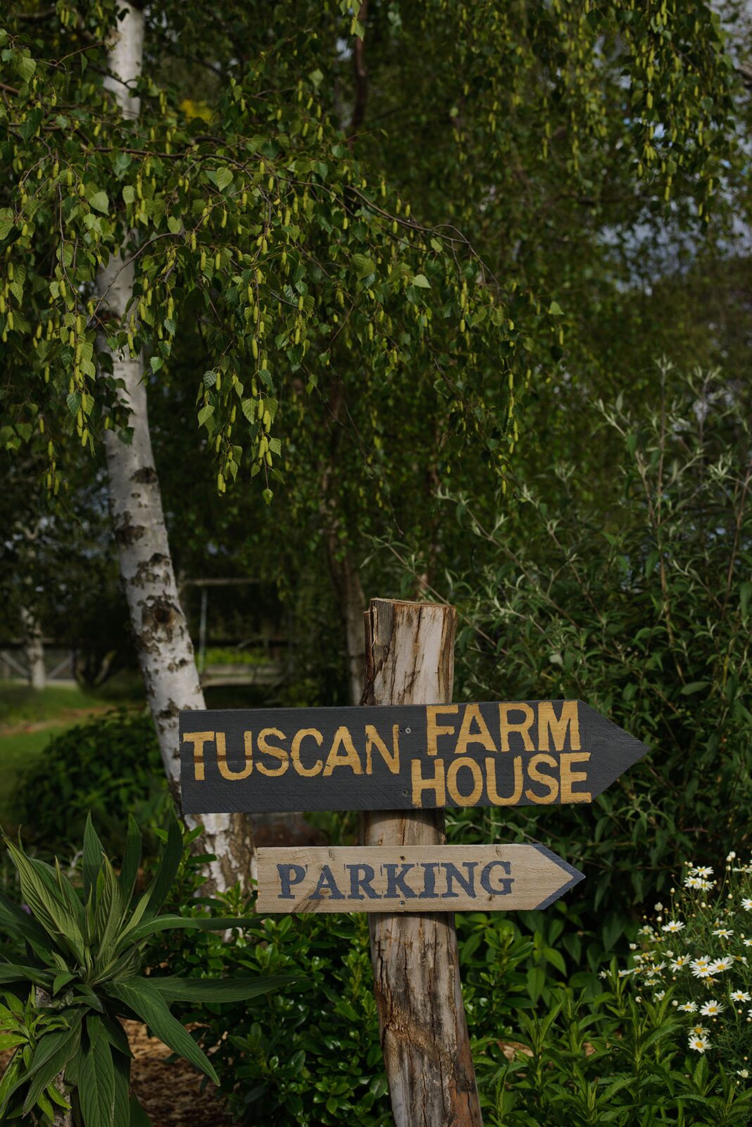 A wooden signpost with a black arrow pointing to the right, indicating the direction to Tuscan Farm House and a parking area.