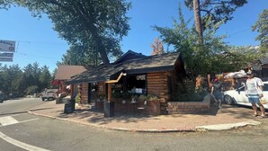 A rustic log cabin-style building with a 'OPEN' sign, outdoor seating, and a visible address number.