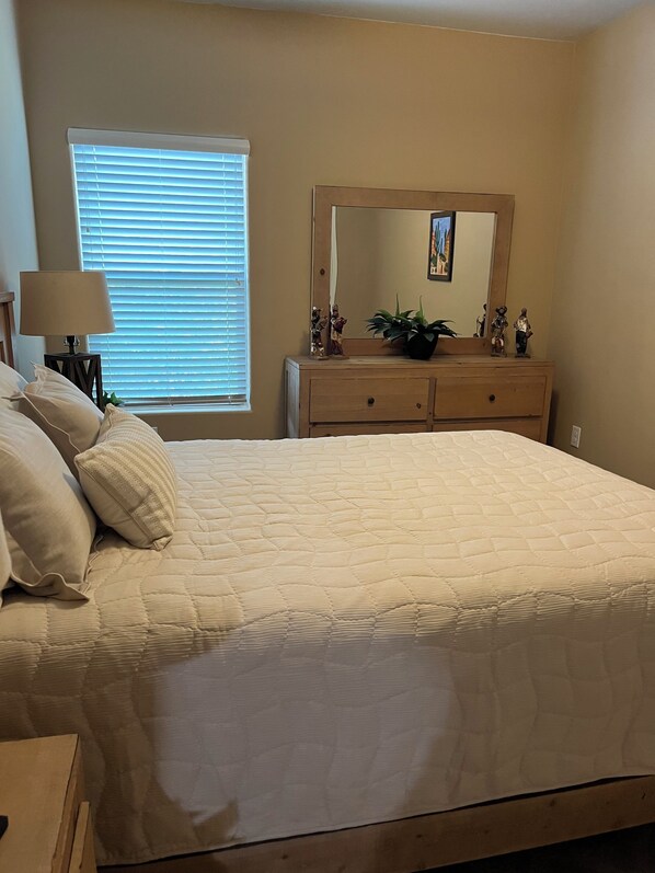 A bedroom with a bed, a dresser, a mirror, a window with blinds, and a lamp.