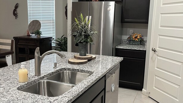 A modern kitchen with granite countertops, stainless steel appliances, and dark cabinetry. - Saguaro Bloom Beauty (Marana)