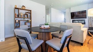 A modern living room with a round wooden table, four grey chairs, a beige sofa, and a television mounted on the wall. - Downtown Charm Meets Waterfront Walk to Everything (Vancouver)
