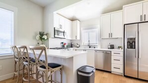 Una cucina moderna con mobili bianchi, un frigorifero in acciaio inossidabile, un forno integrato e un'area con sgabelli da bar.