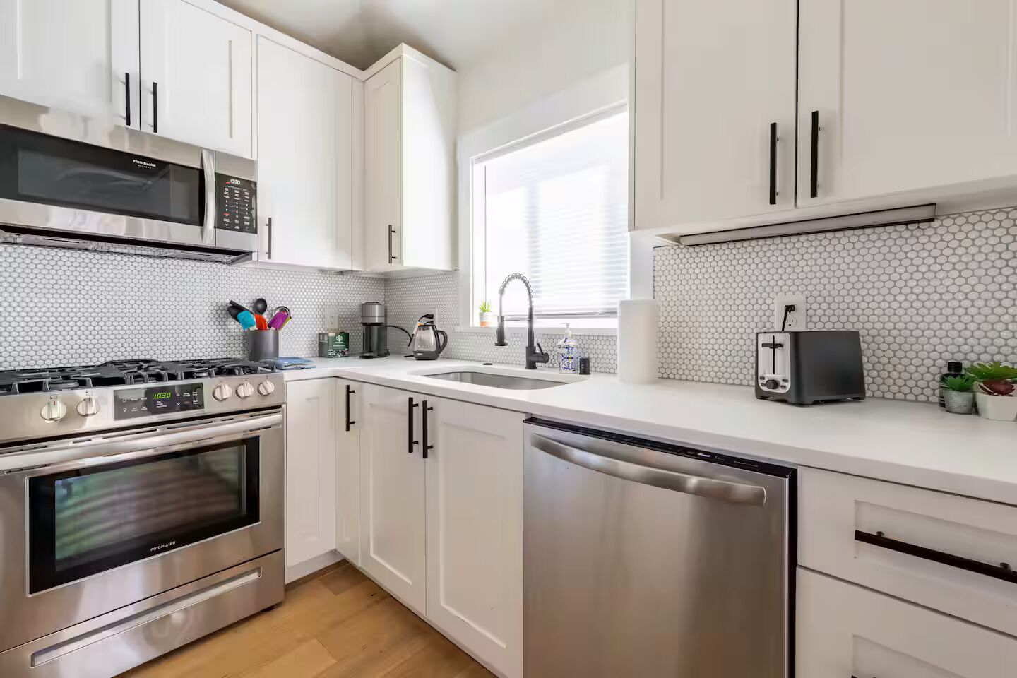 A modern kitchen with white cabinets, stainless steel appliances, a microwave, stove, dishwasher, and a toaster.