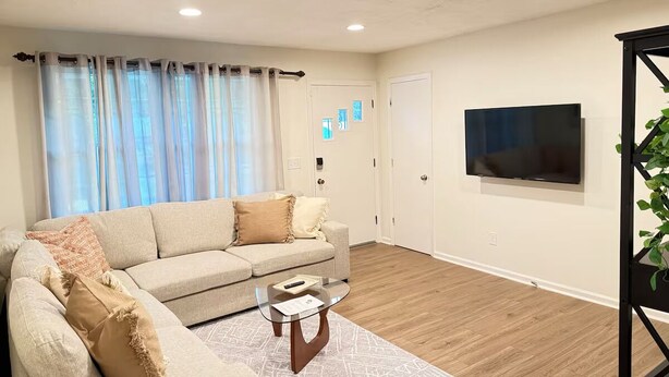 A modern living room with a beige sofa, a glass coffee table, and a flat-screen TV mounted on the wall.