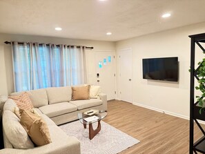 Una sala de estar moderna con un sofá color beige, una mesa de centro de vidrio y un televisor de pantalla plana montado en la pared.