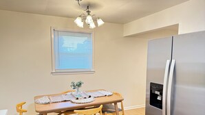 A dining area with a wooden table, four chairs, a vase with a plant, and a stainless steel refrigerator.