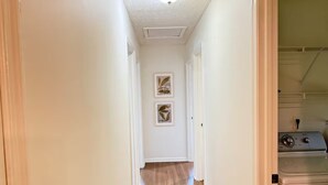 A hallway with wooden flooring, white walls, and a laundry area with a washing machine.