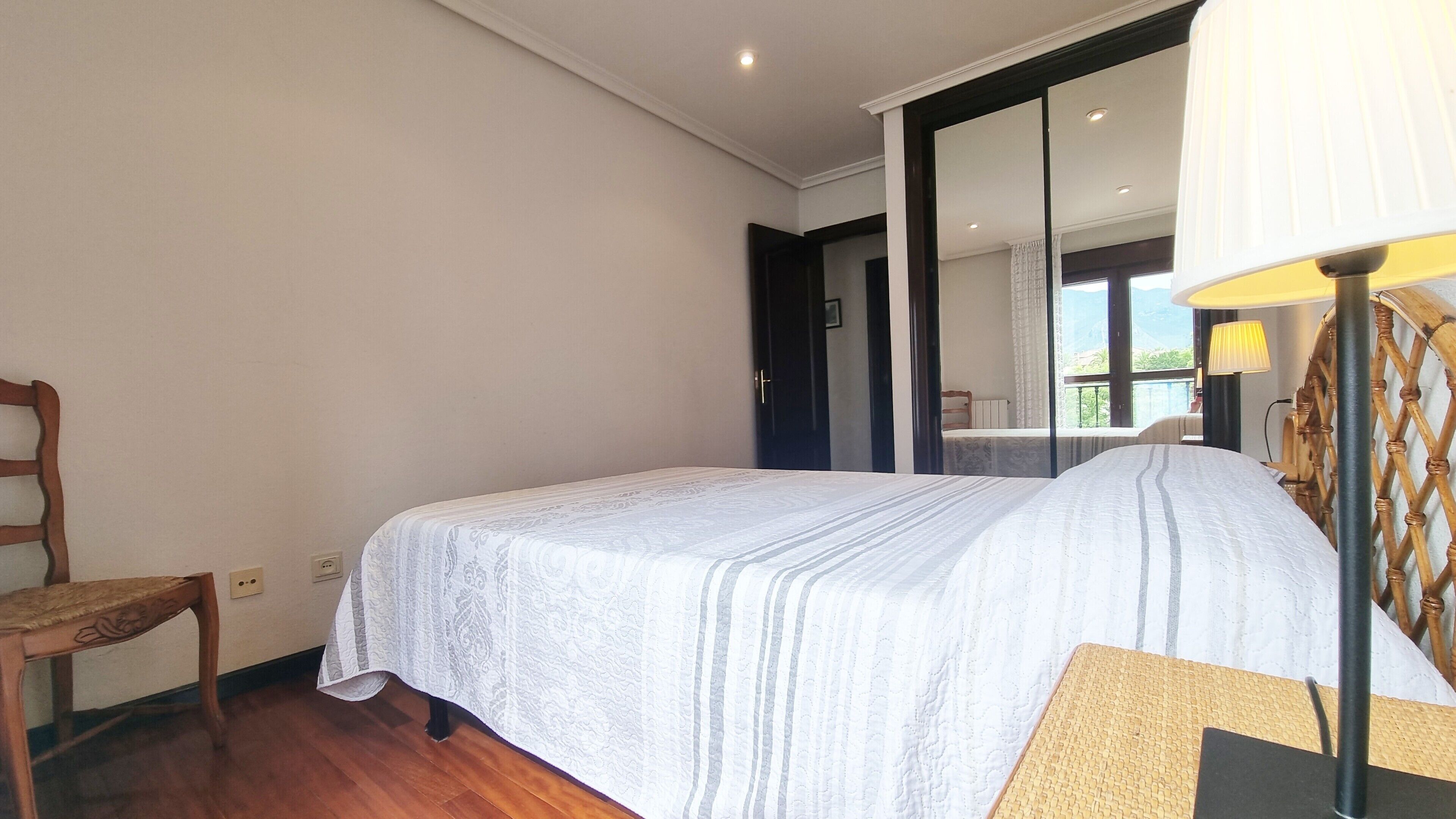 Un dormitorio con cama, una silla, una lámpara y un espejo grande.