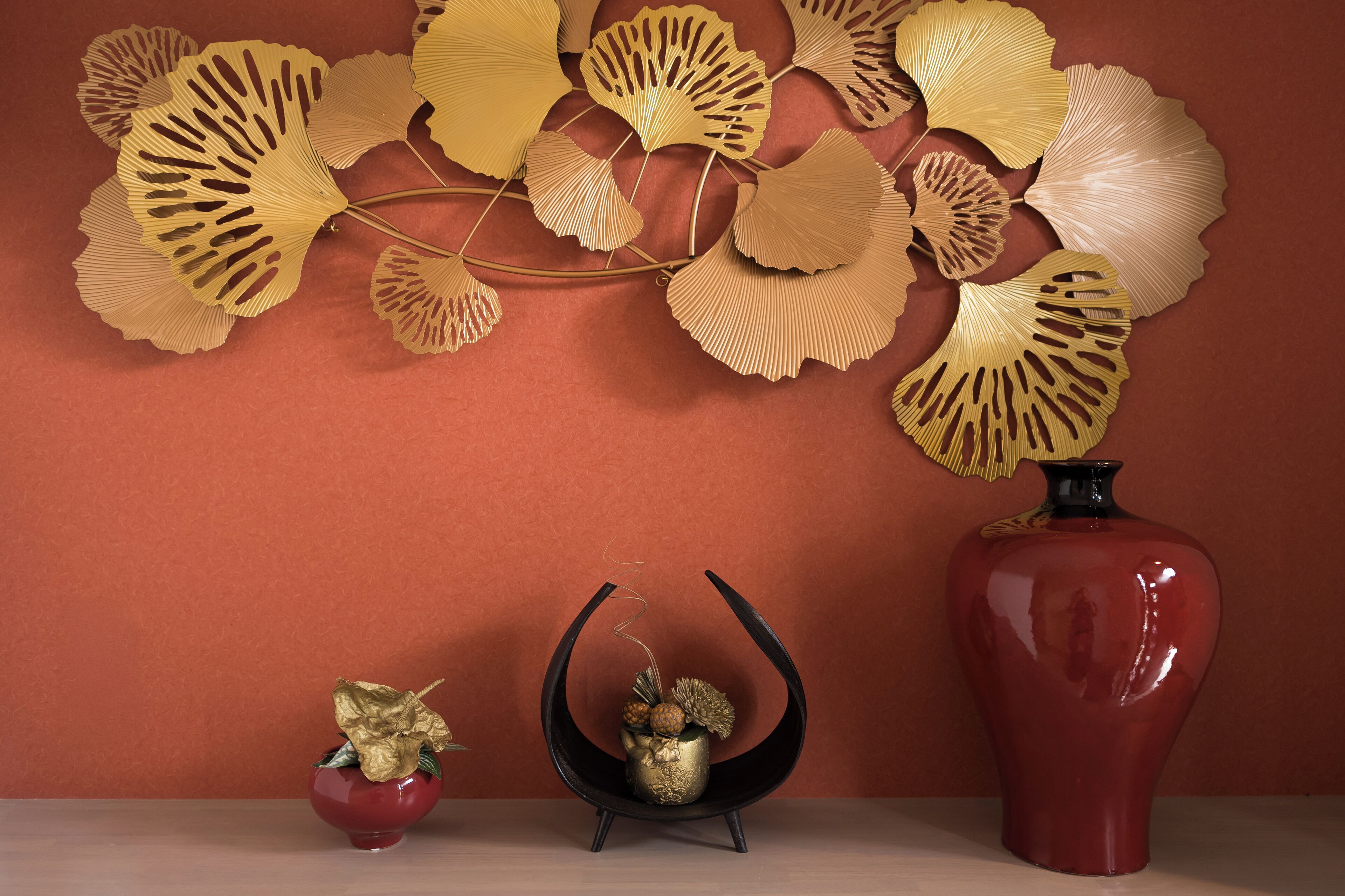 A decorative arrangement with a red vase, a black curved stand, and a small red bowl with a golden leaf.