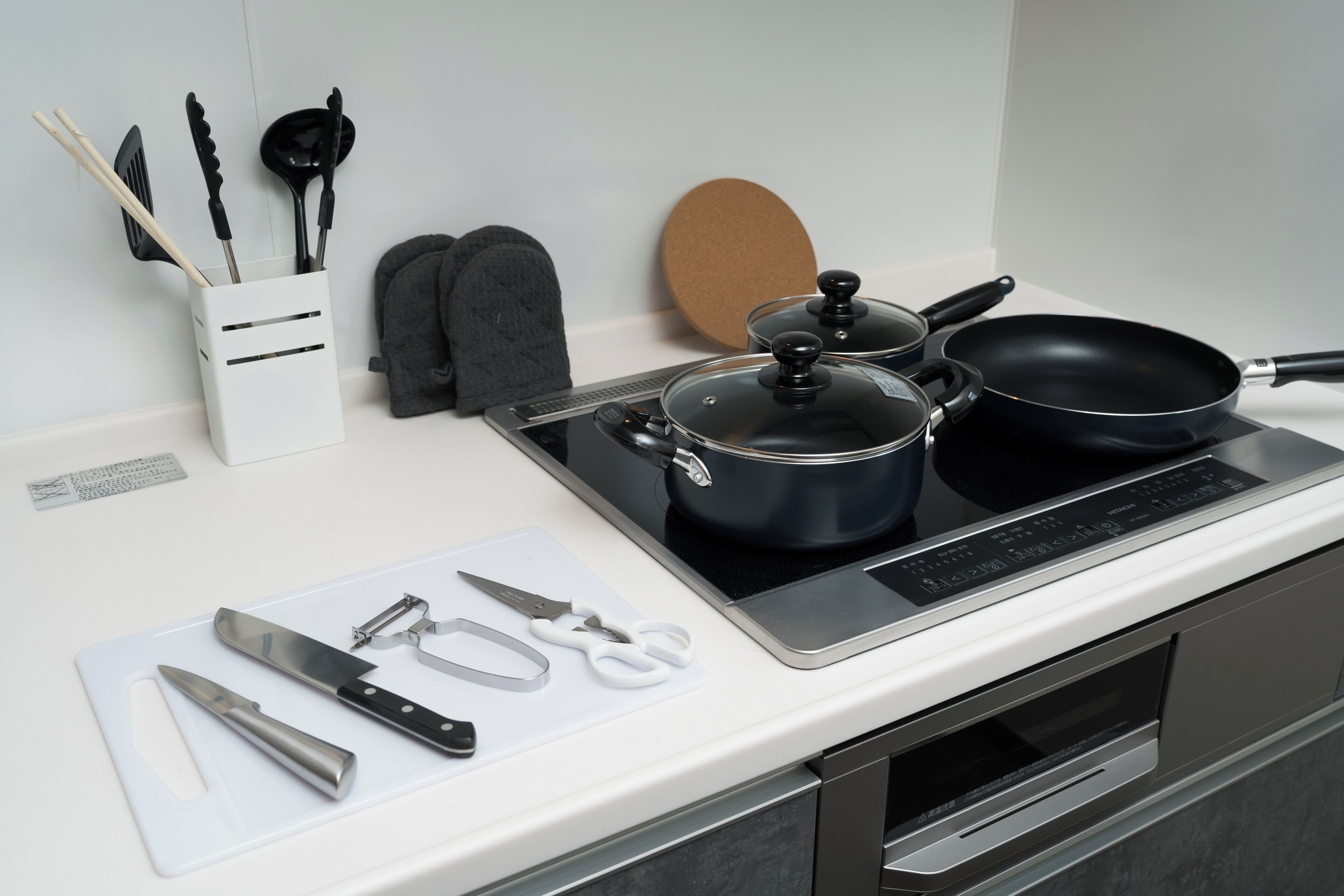 Una cocina con estufa, ollas, una sartén y varios utensilios sobre la encimera.