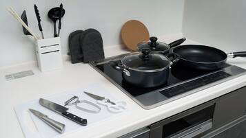 Una cocina con estufa, ollas, una sartén y varios utensilios sobre la encimera.