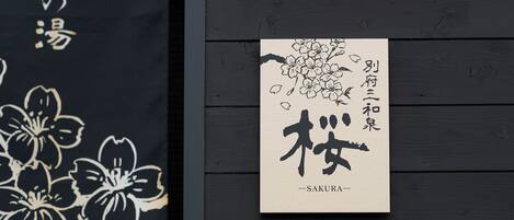 A framed piece of artwork with Japanese calligraphy and a floral design, mounted on a dark wooden wall.
