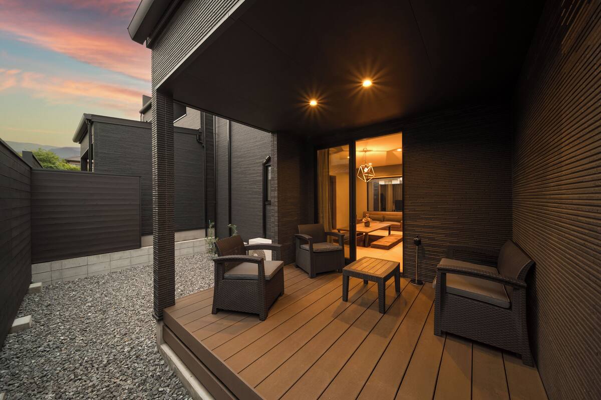 Een terras buiten met rieten meubilair, een tafel en uitzicht op het interieur door een glazen deur.