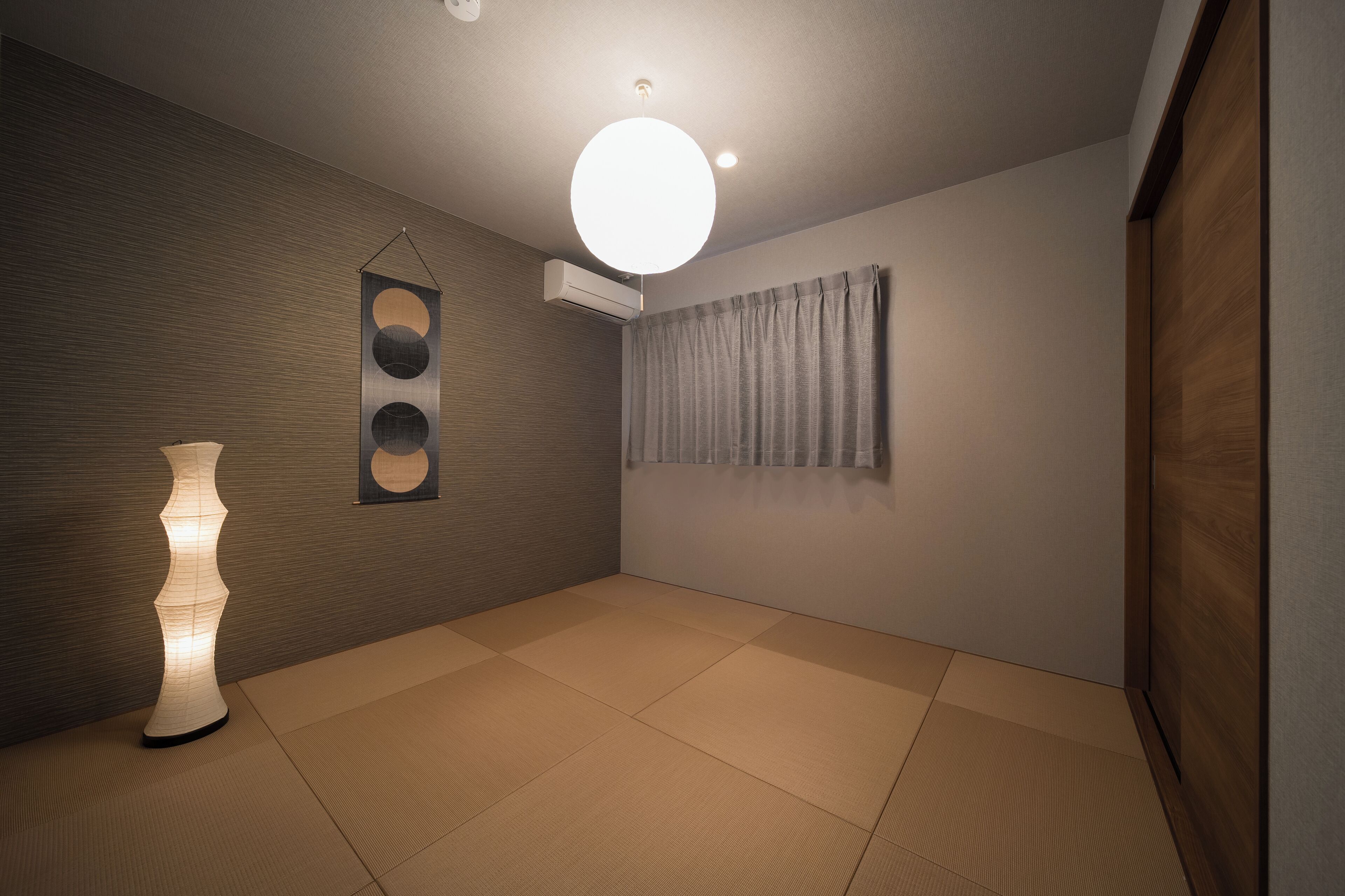 Una habitación con suelo de tatami, lámpara colgante, aire acondicionado instalado en la pared y una cortina.