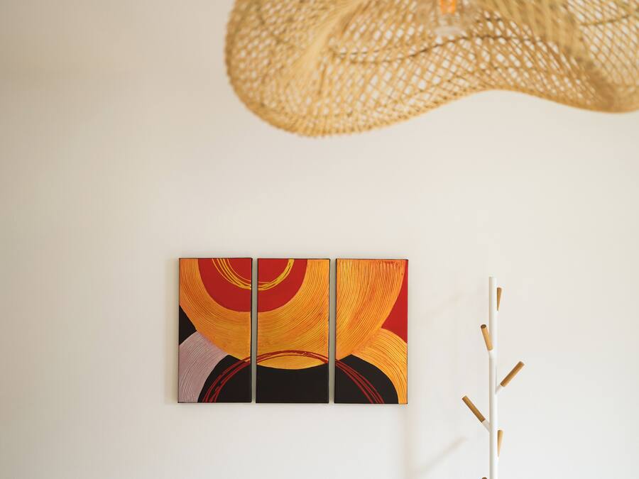 Een muur met een drieluik abstract schilderij en een witte, verticale, minimalistische sculptuur.
