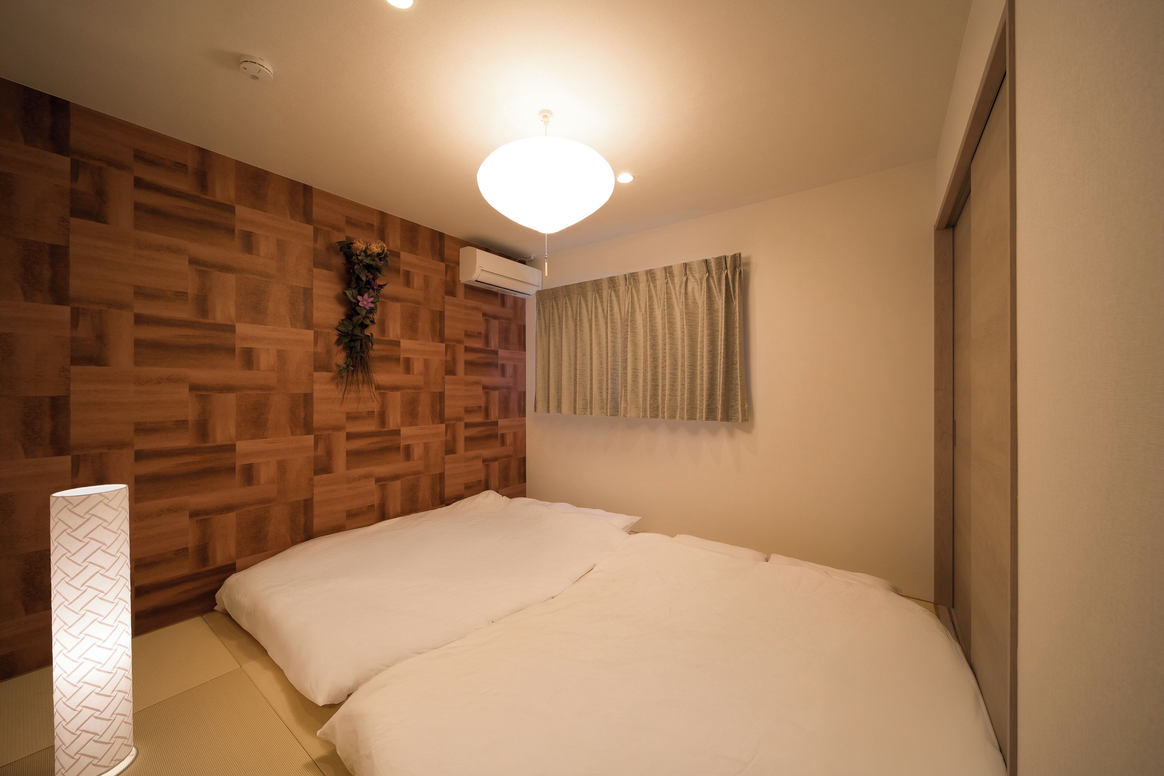 Une chambre avec un lambris en bois, un lit avec une literie blanche, une plante suspendue et un luminaire au plafond.