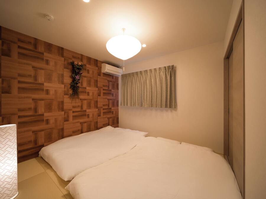 Un dormitorio con un panel de pared de madera, una cama con ropa blanca, una planta colgante y una lámpara de techo.